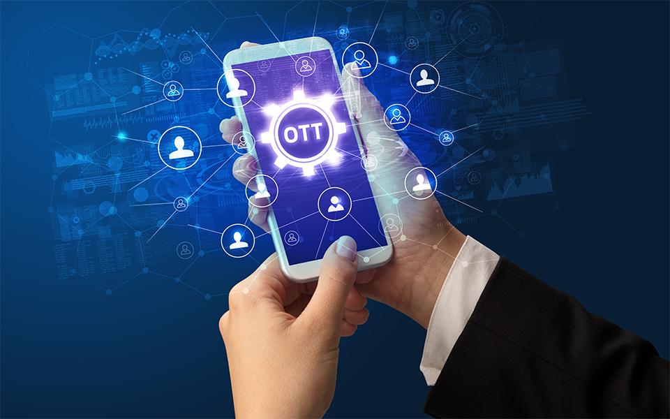 A smartphone held by a businessperson displaying "OTT" on the screen, surrounded by digital network icons and data visualizations in a futuristic blue background.